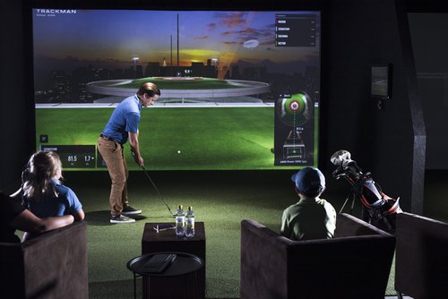 Man in athletic attire swinging a golf club at a driving range simulator, focusing on his form and technique